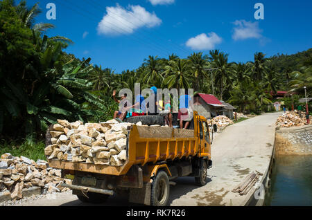 I giovani filippini lavoratore costruzione boy sventolare dal retro di un camion pieno di rocce - Romblon, Filippine