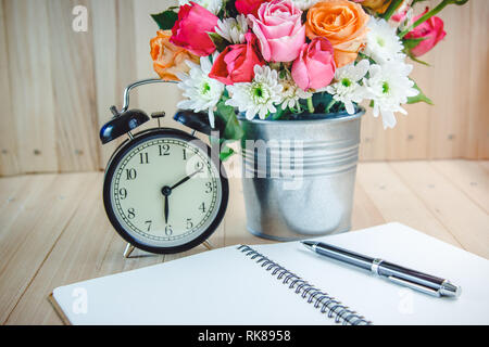 Vaso di bouquet di rose in alluminio con benna nero orologio vintage. Mettere la penna sul nootbookon tavolo in legno, set di bellissimi fiori Foto Stock