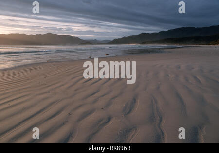 Cox morso dell'ultima luce. Il sole tramonta su di una spiaggia deserta nel Sud Tasmania, dove la costa sud via passa. Tracciare la costa frastagliata di Tas Foto Stock