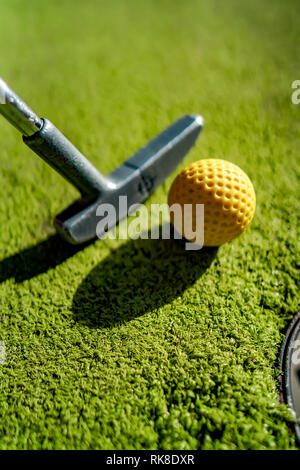 Mini Golf sfera gialla con un bat in prossimità del foro al tramonto Foto Stock