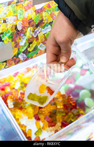 Bambino prende mano caramelle gommose dalla vetrina sul negozio di dolci. Close up caramelle colorate con lo zucchero. Foto Stock