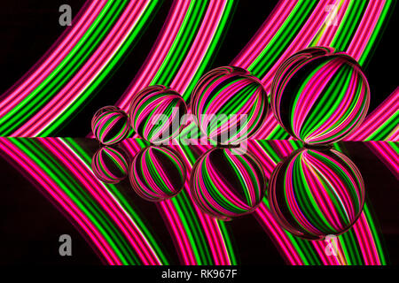 Quattro diverse dimensioni crystal / Vetro / lente di palline in una fila riflettendo come in uno specchio su un fondo nero con rosa e verde della luce al neon striature dietro Foto Stock