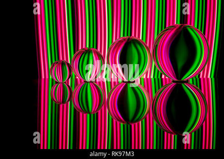 Quattro diverse dimensioni crystal / Vetro / lente di palline in una fila riflettendo come in uno specchio su un fondo nero con rosa e verde della luce al neon striature dietro Foto Stock