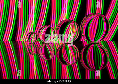 Quattro diverse dimensioni crystal / Vetro / lente di palline in una fila riflettendo come in uno specchio su un fondo nero con rosa e verde della luce al neon striature dietro Foto Stock