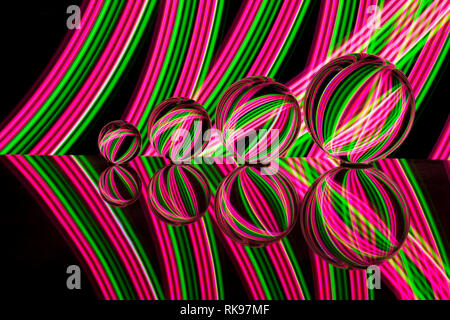 Quattro diverse dimensioni crystal / Vetro / lente di palline in una fila riflettendo come in uno specchio su un fondo nero con rosa e verde della luce al neon striature dietro Foto Stock