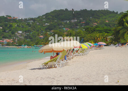 Lettini da sole e ombrelloni sulla spiaggia di sabbia. St George, Grenada Foto Stock