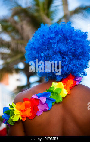 Vivacemente colorato rainbow ghirlanda di fiori e blu parrucca afro su un irriconoscibile l uomo a un carnevale brasiliano street party in Rio de Janeiro, Brasile Foto Stock