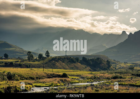 I raggi di luce streak attraverso i bordi frastagliati dell'Anfiteatro montagna nel Drakensberg, Sud Africa Foto Stock