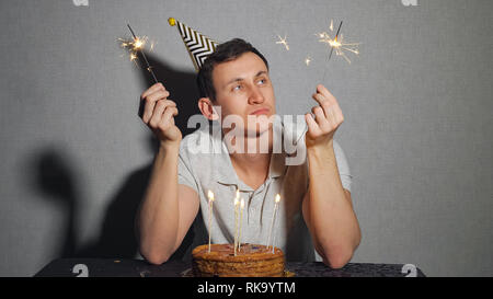 Triste Lonely Man in party hat festeggia il compleanno da sola e tenendo il sparkler Foto Stock
