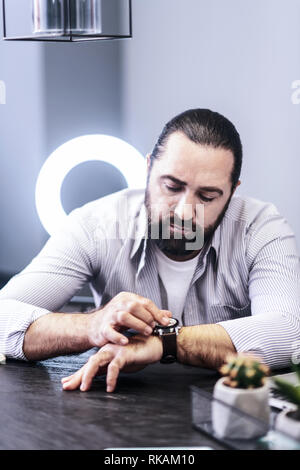 Dai capelli scuri uomo barbuto in una camicia a righe controllando il suo orologio Foto Stock