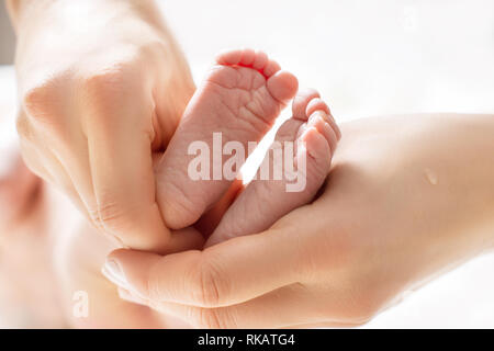 Mom massaggi gambe di un bambino di neonato. Piedi del bambino nelle mani di madre. Piccola nuova data di nascita del bambino in piedi sulle mani femminili closeup Foto Stock