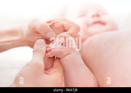 Mom massaggi gambe di un bambino di neonato. Piedi del bambino nelle mani di madre. Piccola nuova data di nascita del bambino in piedi sulle mani femminili closeup. La mamma e il suo bambino. La felicità Foto Stock