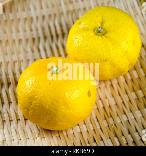 Due yuzu frutti (un aspro e fragrante giapponese varietà di agrumi) su un cesto tessuto Foto Stock