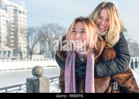 Amiche sono sciocchezze intorno, saltando su ogni altro spalle mentre si cammina attraverso un winter park vicino a un fiume congelato Foto Stock