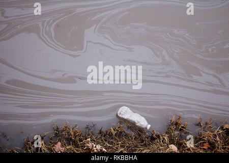 Un scartato una bottiglia d'acqua galleggianti in un flusso inquinato. Foto Stock