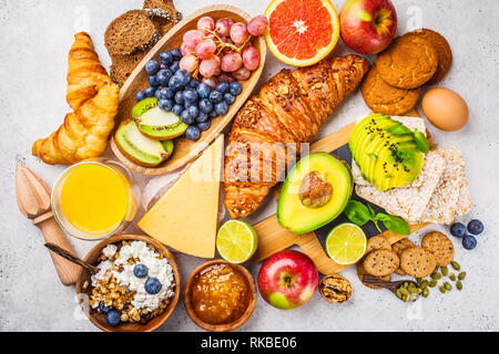 Una sana prima colazione bilanciata su uno sfondo bianco. Muesli, succo di frutta, croissant, formaggio, biscotti e frutta, vista dall'alto. Foto Stock