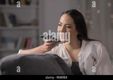 La donna nella notte utilizzando phone il riconoscimento vocale seduto su un divano nella notte a casa Foto Stock