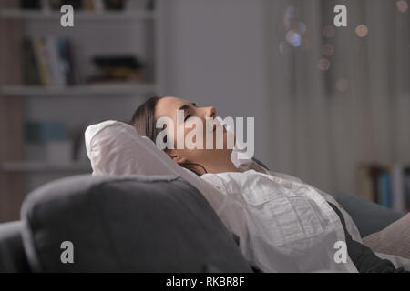 Vista laterale ritratto di una donna appoggiato comodamente seduto su un divano nella notte a casa Foto Stock