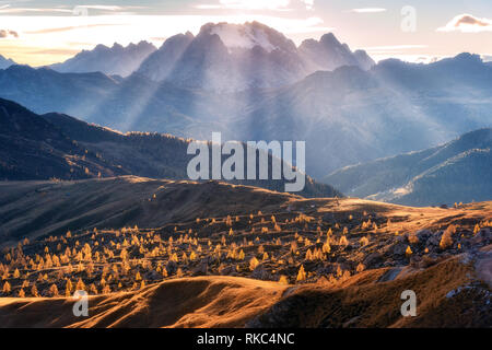 Valle di montagna illuminato con luminosi raggi di sole al tramonto in autunno nelle Dolomiti, Italia. Paesaggio con montagne, colline con alberi di arancio e gr Foto Stock