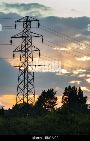 Elettricità pilone con il sole che sorge dietro la creazione di un cielo arancione. Foto Stock