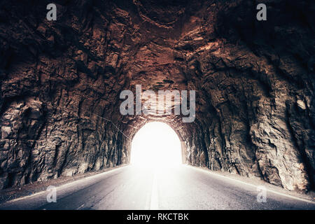 Rocky Tunnel in pietra con luce a fine strada grotta di fuga drammatica pareti grigio rosso Foto Stock