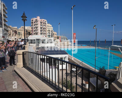 I turisti fotografare lungo la passeggiata sul mare nella baia di St Julians Malta in una giornata di sole Foto Stock