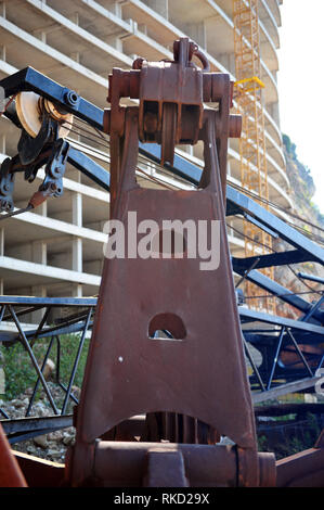 Primo piano verticale della gru di fronte hotel abbandonato in Montengro. Edificio incompiuto con rusty macchina di fronte. Foto Stock