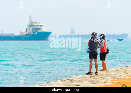 I pescatori pesca dalla diga del porto di Singapore. Commerciale di navi da carico in background Foto Stock