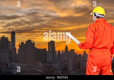 Gli ingegneri asiatici lavoratore tenendo il progetto per la costruzione del paesaggio urbano di sunrise sfondo, concetto industriale Foto Stock