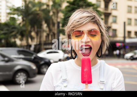 Breve donna dai capelli in zone urbane, cityscape mangiare ghiaccioli. Foto Stock