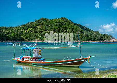 Un Thai long tail pesca barca ancorata a terra in una bellissima isola bay ubicazione. Foto Stock