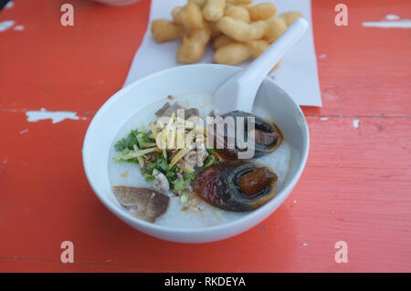 Una zuppa di riso o crema di carne macinata di maiale e interiora con conserva di uovo da scherzo kun pa ristoranti a Amphoe Pak Chong , Korat ,Thailandia Foto Stock