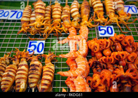 Una disposizione di spiedini di pesce alla griglia consistente di calamari, polpi, calamari e gamberi sbucciato Thai street food snack e stuzzichini in un pesce m Foto Stock