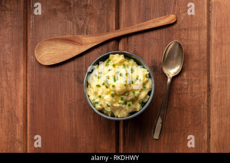 Pomme purea, una foto aerea di una tazza di purea di patate con erbe aromatiche, girato dalla parte superiore su un sfondo rustico con un cucchiaio di legno e spazio di copia Foto Stock