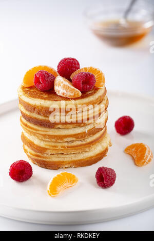 American dolce casalingo pila di pancake o le frittelle con frutti di lamponi e miele, deliziosi dessert per colazione, su sfondo bianco selettivo. Foto Stock