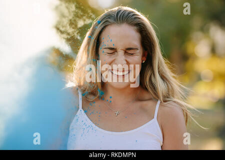 Donna sorridente chiudendo gli occhi durante la riproduzione di holi. Holi color powder gettata su di una donna sorridente. Foto Stock