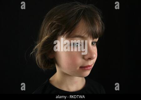 Ritratto di un green eyed marrone ragazza dai capelli visto dal lato contro uno sfondo nero Foto Stock