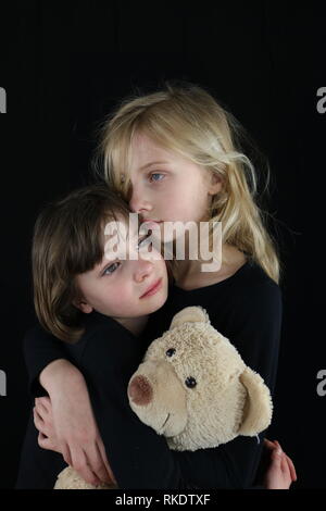 Due giovani sorelle che abbraccia ogni altra nel dolore mantenendo orsacchiotto Foto Stock