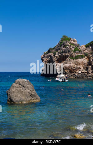 Le persone godono di una calda giornata estiva in acqua tra le formazioni rocciose a Cala Deia Beach in Mallorca, Spagna. Foto Stock