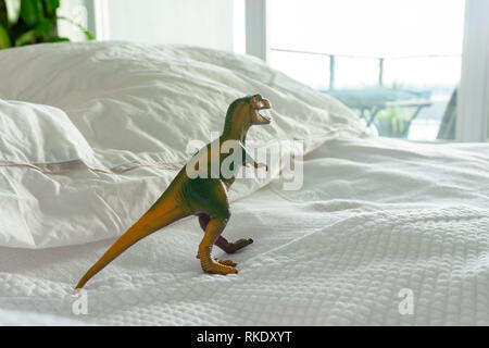 Verde e giallo dinosauro di plastica giocattolo sul letto con i genitori che raffigura una casa famiglia dove i bambini vivono, o la vita di parenting, divertendosi, fantasia etc. Foto Stock