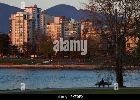 Un uomo si siede su una panchina nel parco in Vanier Park si affaccia su False Creek e Sunset Beach in Vancouver, British Columbia, Canada Foto Stock