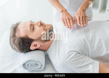 Angolo di alta vista di uomo barbuto ricevendo trattamento reiki Foto Stock