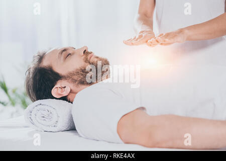 Ritagliato colpo di uomo barbuto con gli occhi chiusi ricevendo trattamento reiki sul petto Foto Stock