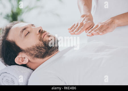 Ritagliato colpo di calma uomo barbuto con gli occhi chiusi ricevendo trattamento reiki Foto Stock