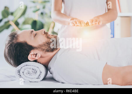 Vista laterale di calma uomo barbuto con gli occhi chiusi ricevendo trattamento reiki Foto Stock