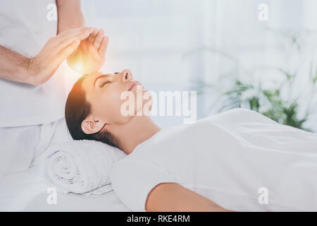 Ritagliato colpo di giovane donna ricevendo la terapia reiki sopra la testa Foto Stock