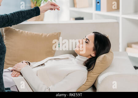 Ritagliato colpo di ipnotizzatore con pendolo ipnotizzanti giovane donna disteso sul lettino Foto Stock