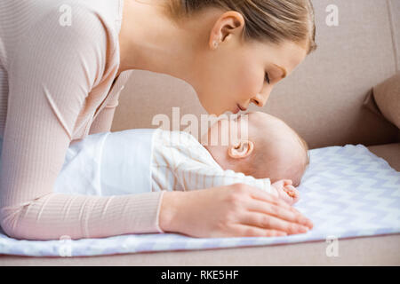 Vista laterale di felice giovane madre baciare adorabile bambino sdraiato sul lettino Foto Stock