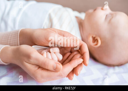 Ritagliato colpo di madre tenendo una mano sul neonato adorabile bambino sdraiato sul divano Foto Stock