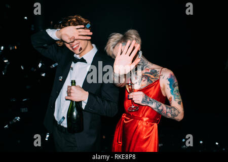 Giovane che ricopre la faccia tenendo alcol bevande sulla parte isolata su nero Foto Stock